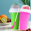 A bright green cup and a pink cup with a spoon are shown next to fresh fruit like oranges, kiwi slices, and cherries.