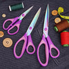 A collection of purple and silver craft scissors and a brown thread spool on dark fabric.