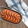 A baked swirl cake in a metal baking tray lined with a striped cloth.