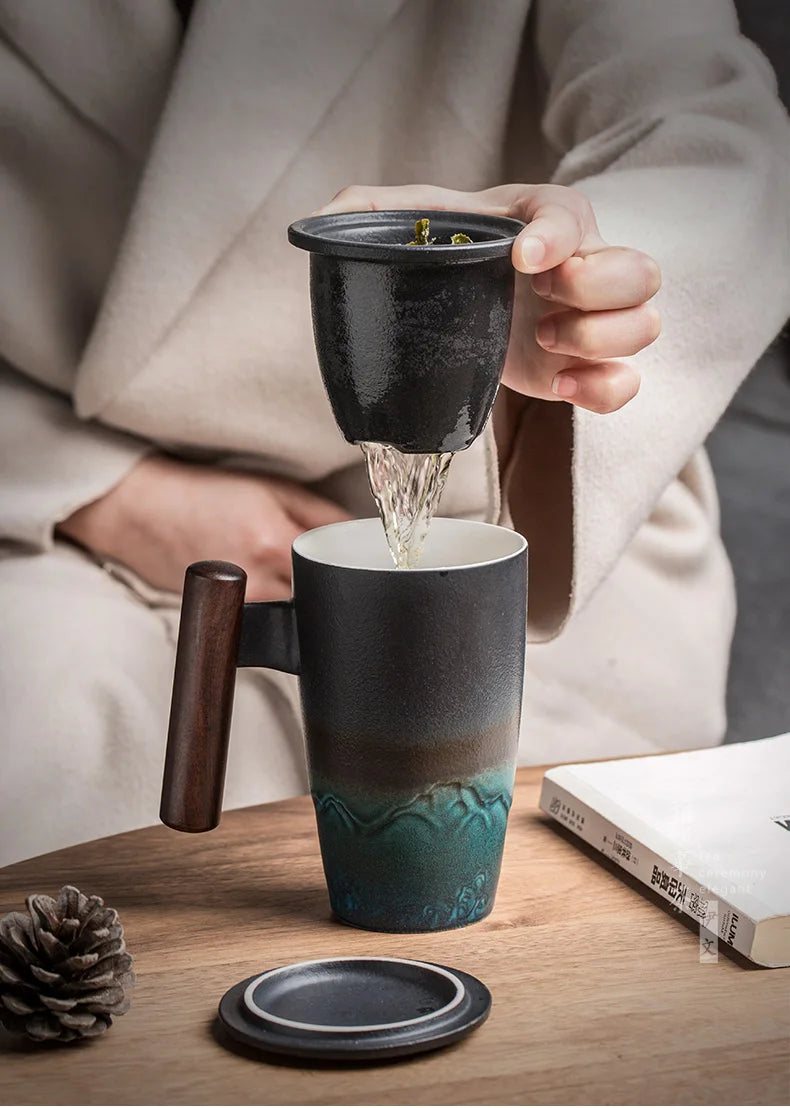 Una mano vierte té de una taza de cerámica a otra, sobre una superficie de madera.