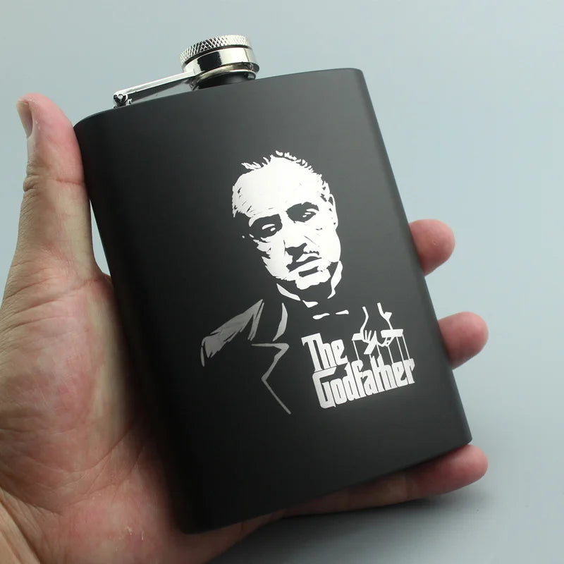 A hand holds a black laser engraved stainless steel hip flask with a silver cap.
