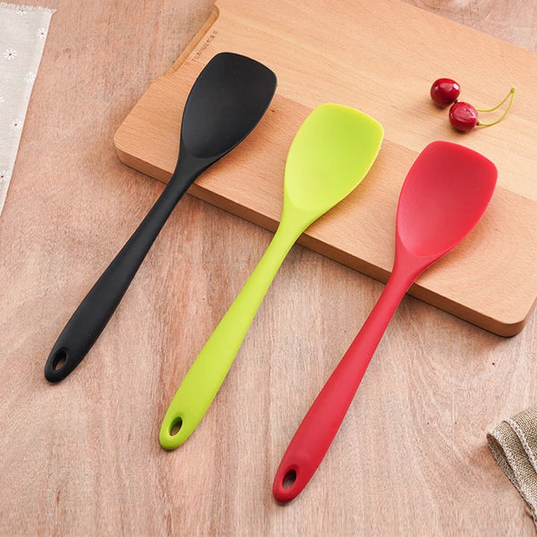 Ein Set aus drei lebensmittelechten Silikon-Kochschneebesen in schwarz, limettengrün und rot auf einem Holzbrett.