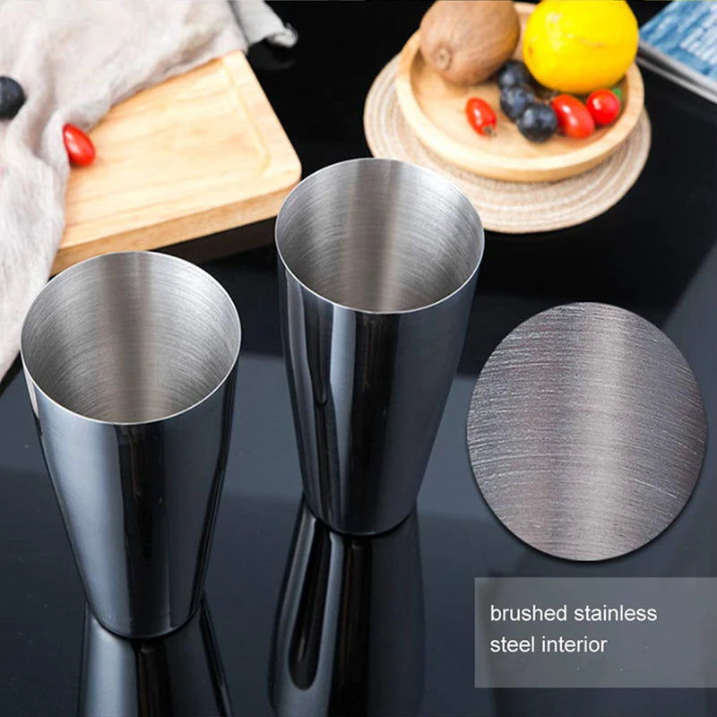 A set of brushed stainless steel cocktail shakers displayed on a black surface with fresh fruit.