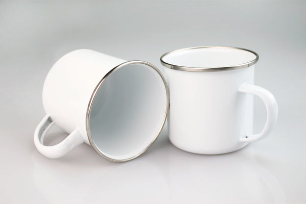 Weiße Emaille-Tasse mit silbernem Rand und Henkel vor hellem grauem Hintergrund