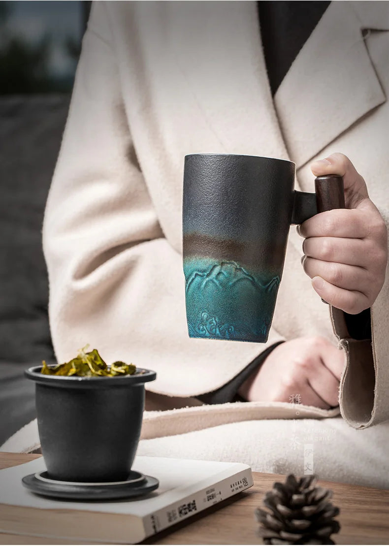 Una persona sostiene una taza de té de cerámica oscura con tapa, junto a una chaqueta beige claro y un libro.