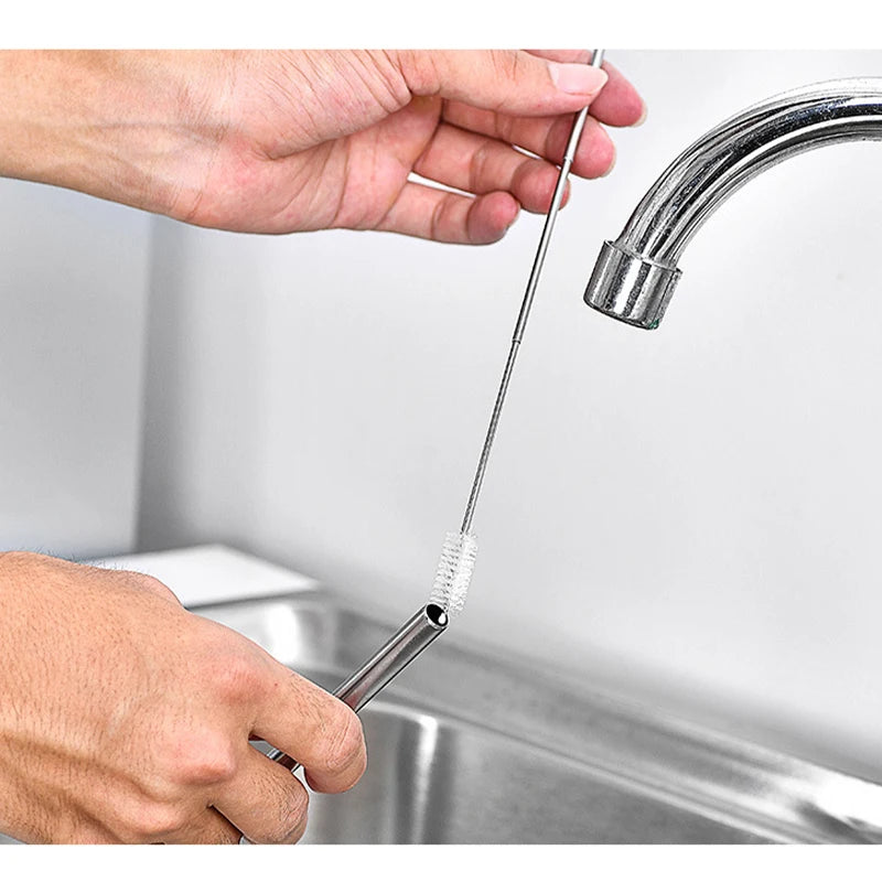 A hand is using a stainless steel telescopic drinking straw with a cleaning brush to clean a kitchen sink.