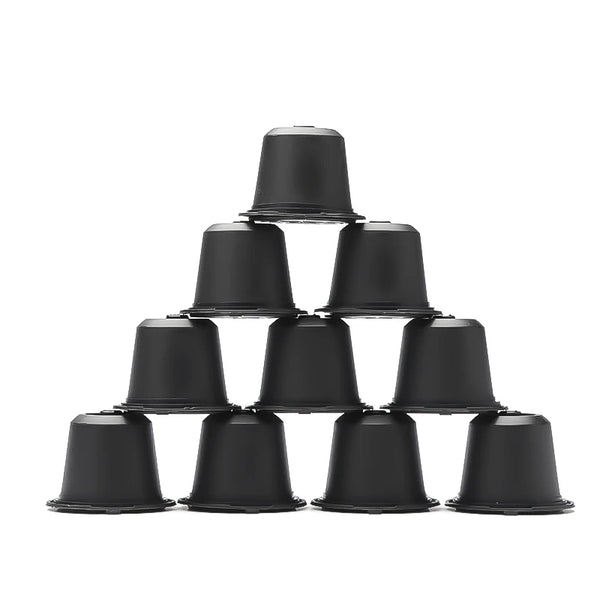 A stack of ten black reusable coffee capsule filters for Nespresso machines with a spoon and brush.