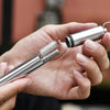 A hand holds a stainless steel telescopic drinking straw with a cleaning brush.