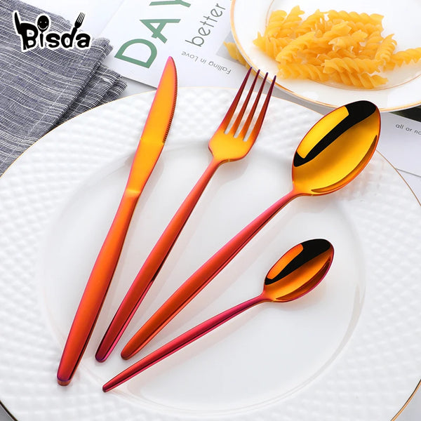 Set an eleganter, glänzender, orangefarbener Edelstahlbesteck mit Messer, Gabel und Löffel auf einer weißen Platte
