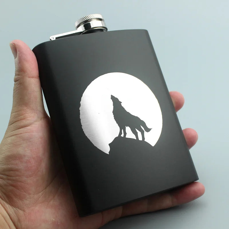 A black laser engraved stainless steel hip flask with a silhouette of a wolf on a moon background.