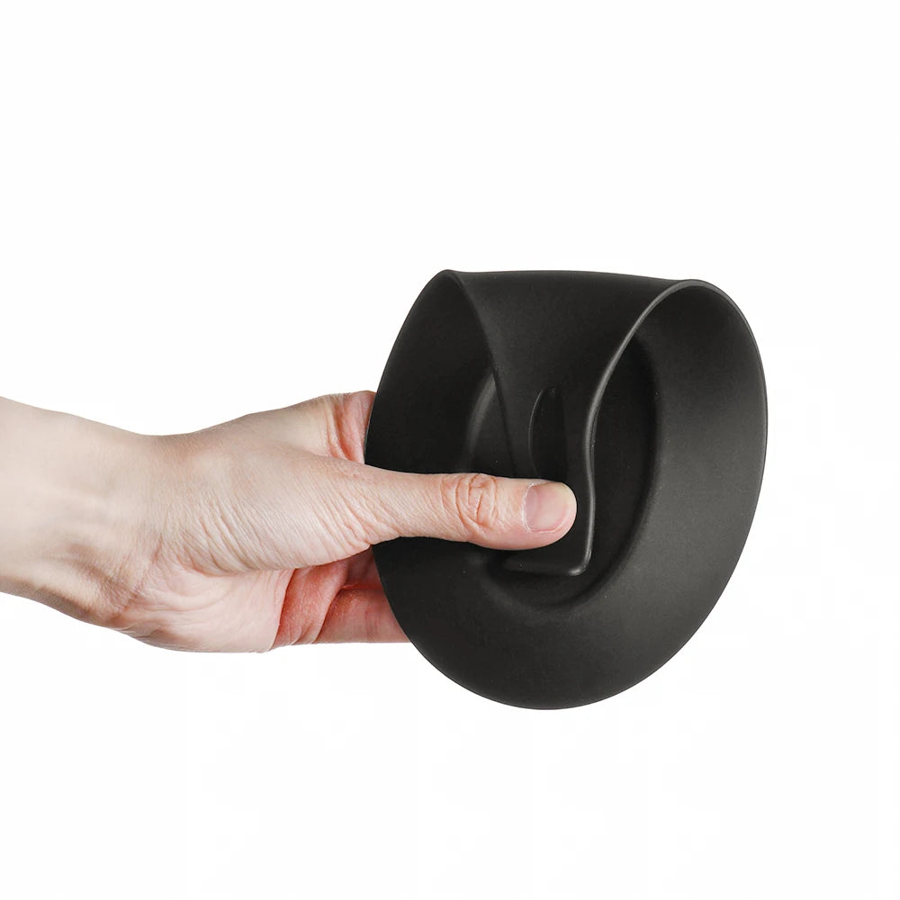 A hand is holding a black silicone utensil holder with a curved design.