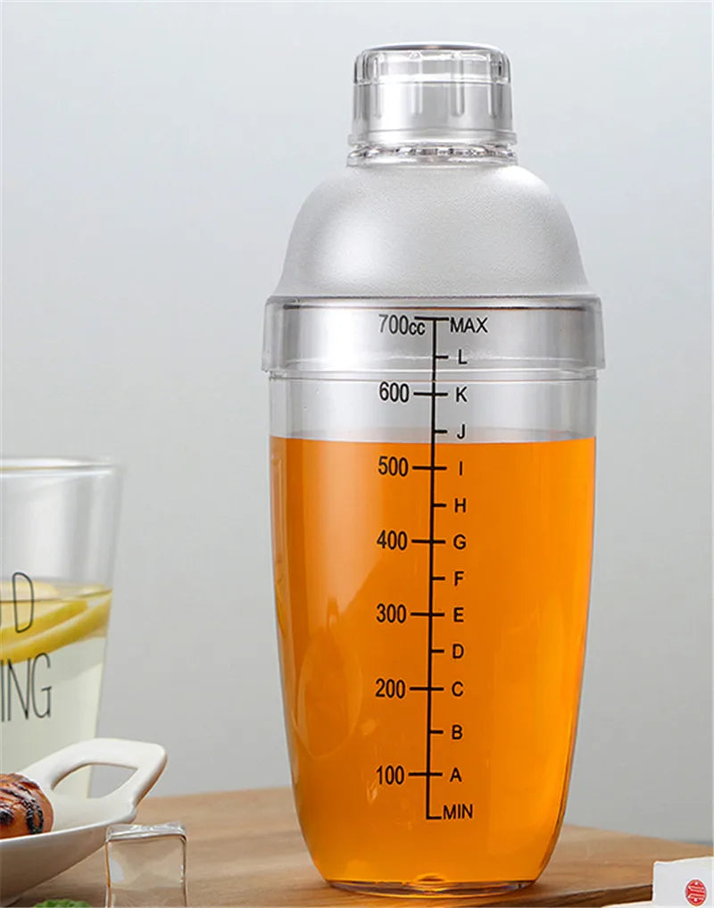 A clear plastic cocktail shaker bottle filled with orange liquid, sitting on a wooden surface.