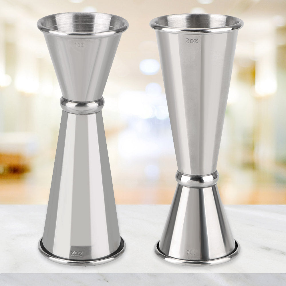 Un couple de jiggers en acier inoxydable poli posés sur une surface de marbre blanc.