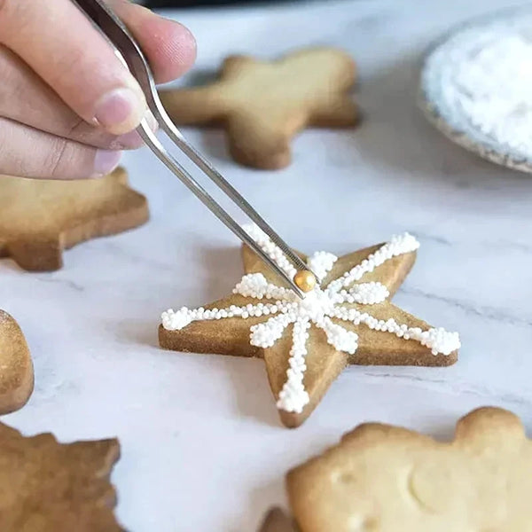Eine Hand benutzt eine Edelstahl-Küchenzange, um einen Lebkuchenstern-Keks mit Puderzucker aufzuheben.