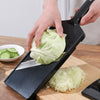 A hand is using a black vegetable grater tool to shred a head of green cabbage on a wooden cutting board.