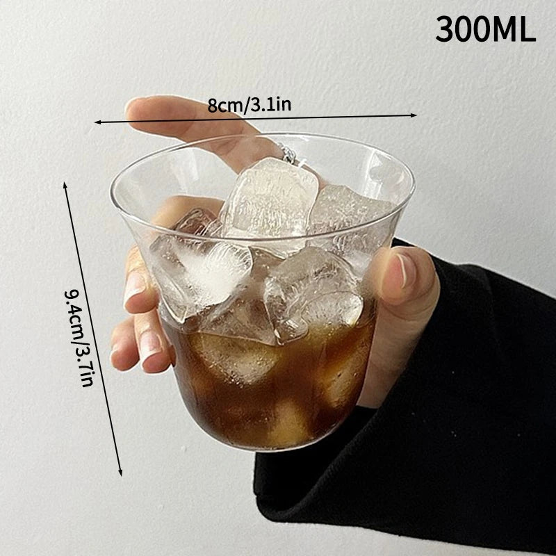 A hand holds a 300ml glass tumbler filled with iced tea or beverage, showing its dimensions.