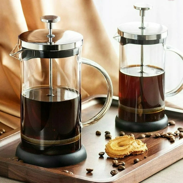 Ein Glas- und Edelstahl-Kaffeepressegefäß mit dunklem, gebrühtem Kaffee steht auf einem Holzbrett.