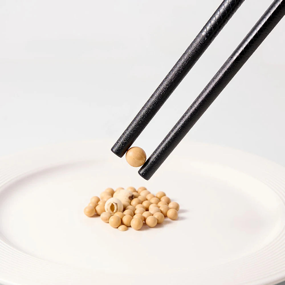 A pair of black chopsticks is dropping a small, light-colored nut onto a white plate.
