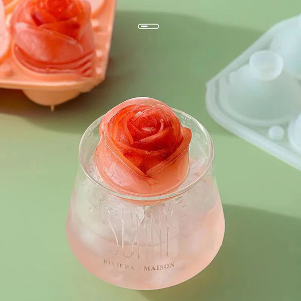 Ein durchsichtiges Glas enthält eine rosa Rosen-Eiswürfelform mit roter Rosen-Design vor einem hellgrünen Hintergrund.