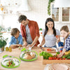 A woman prepares food in a kitchen, with a microwave splash guard lid and fresh vegetables on the table.