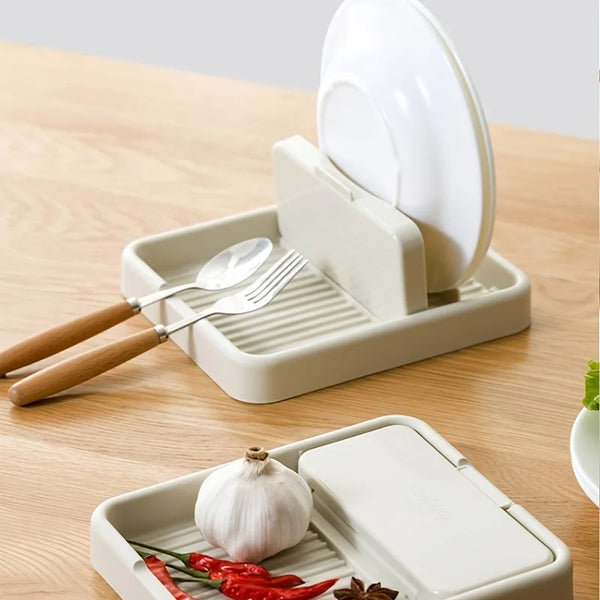 A white kitchen pot lid rack organizer holding a silver spoon and fork, with a whole garlic bulb and chili peppers.
