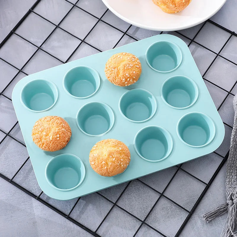 A light blue silicone baking pan set with six cups and five golden-fried pastries arranged on a dark grid surface.