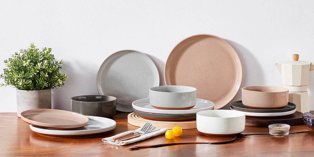 A set of stoneware dinnerware including plates, bowls, and a teapot in earthy tones on a wooden table.