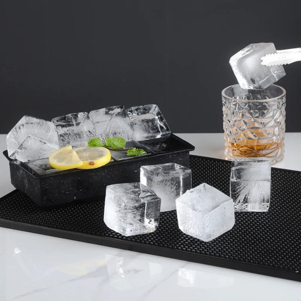 Eine schwarze Schale hält verschiedene klare Eiswürfel, eine Zitronenscheibe und ein Glas bernsteinfarbene Flüssigkeit.