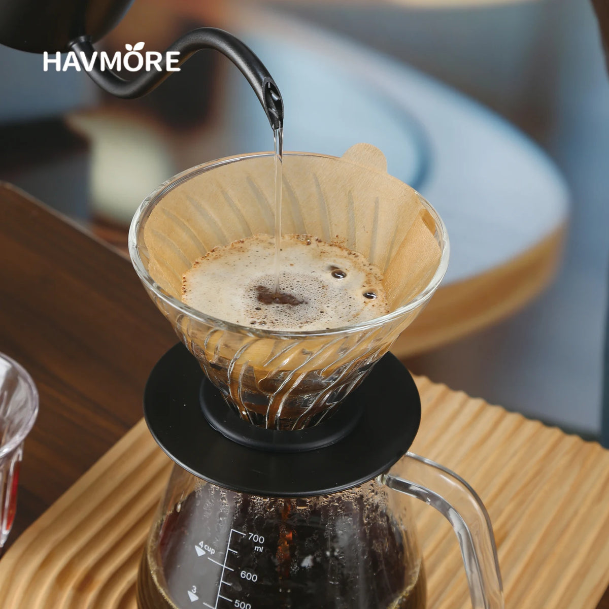 A dark liquid is being poured into a glass filter during a pour over coffee brewing process.