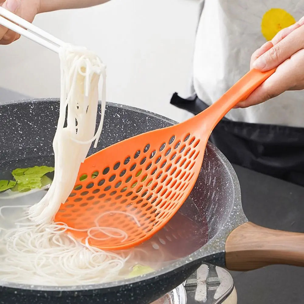 A hand uses an orange kitchen strainer or skimmer to lift white noodles from a pot.