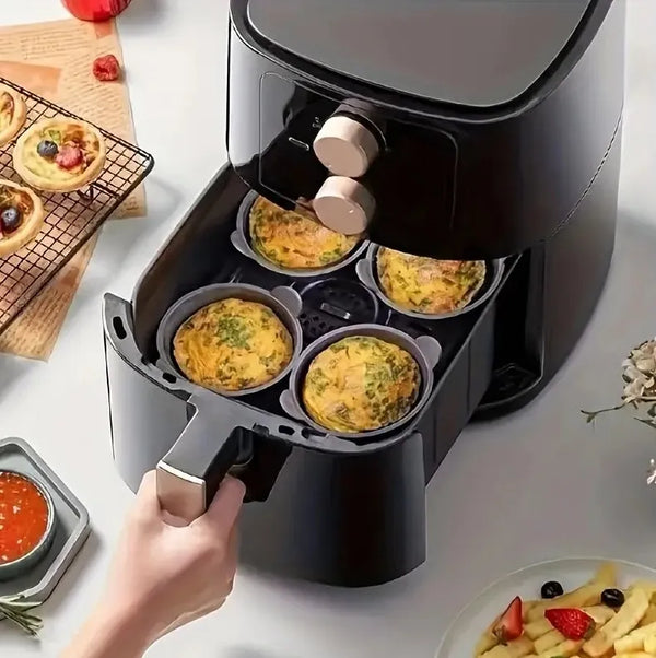 A hand is removing four golden egg poaching cups from a black air fryer or oven appliance.