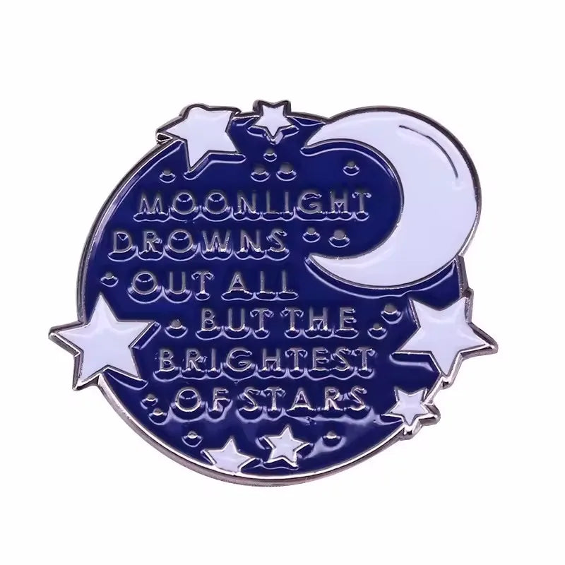 A blue enamel pin featuring a crescent moon and stars with the text Moonlight Downs