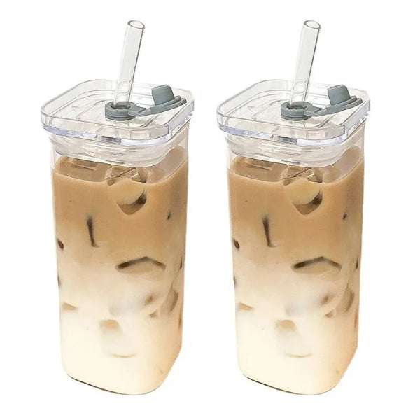Hohe Glas-Tasse mit Eistee oder ähnlichem Getränk, Eiswürfeln und einem klaren Plastikdeckel mit Strohhalm.
