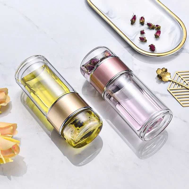 Double-layer borosilicate glass tea infuser with yellow and pink liquid displayed on a marble surface.