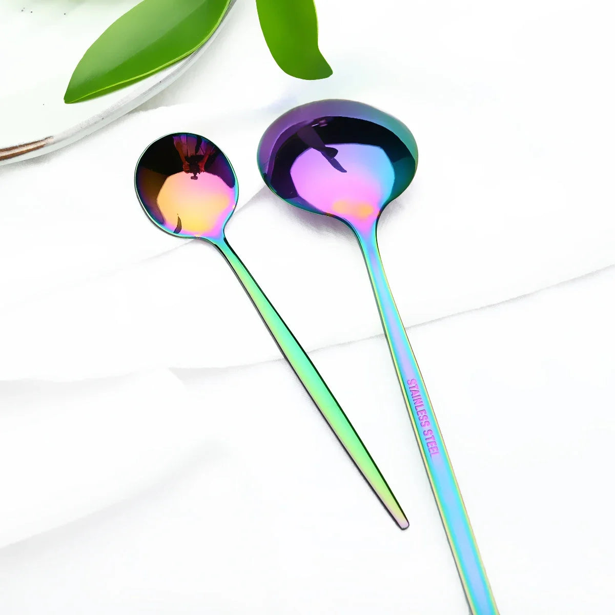 A set of six iridescent purple and green stainless steel cutlery spoons resting on a white cloth.