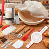 A complete sourdough starter kit featuring a banneton basket, various tools like a peeler, brush, and scraper, laid out on a 