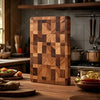 A thick wooden cutting board with a geometric pattern rests on a wooden table in a kitchen setting.
