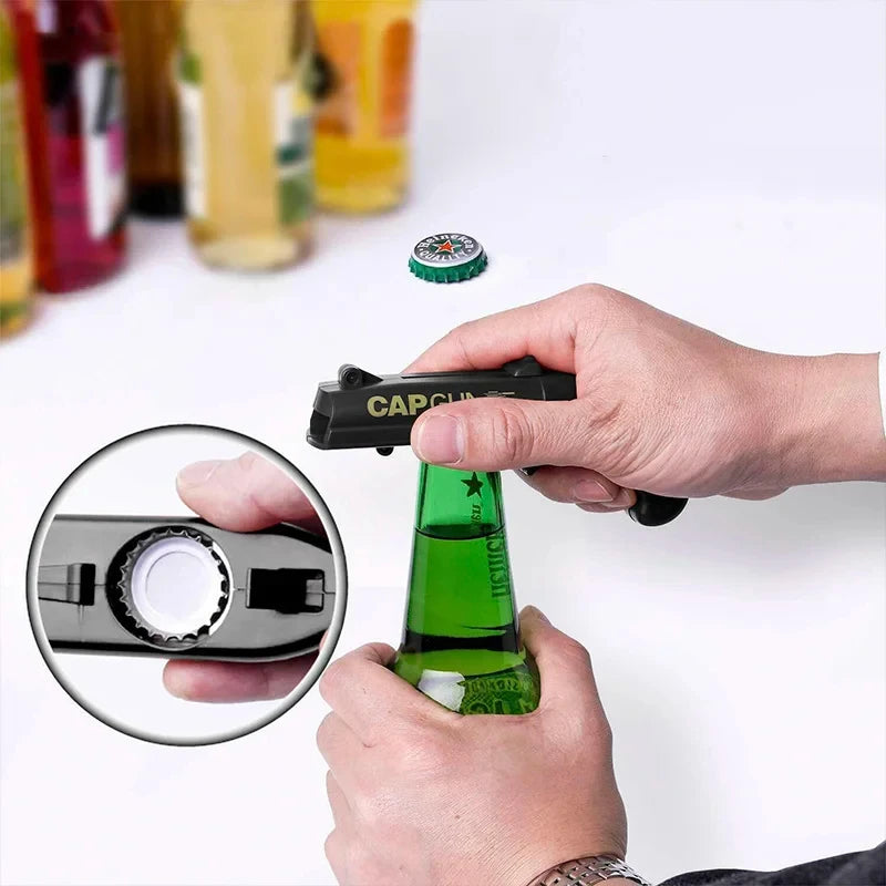 A hand is using a portable bottle opener cap gun to open a green bottle.