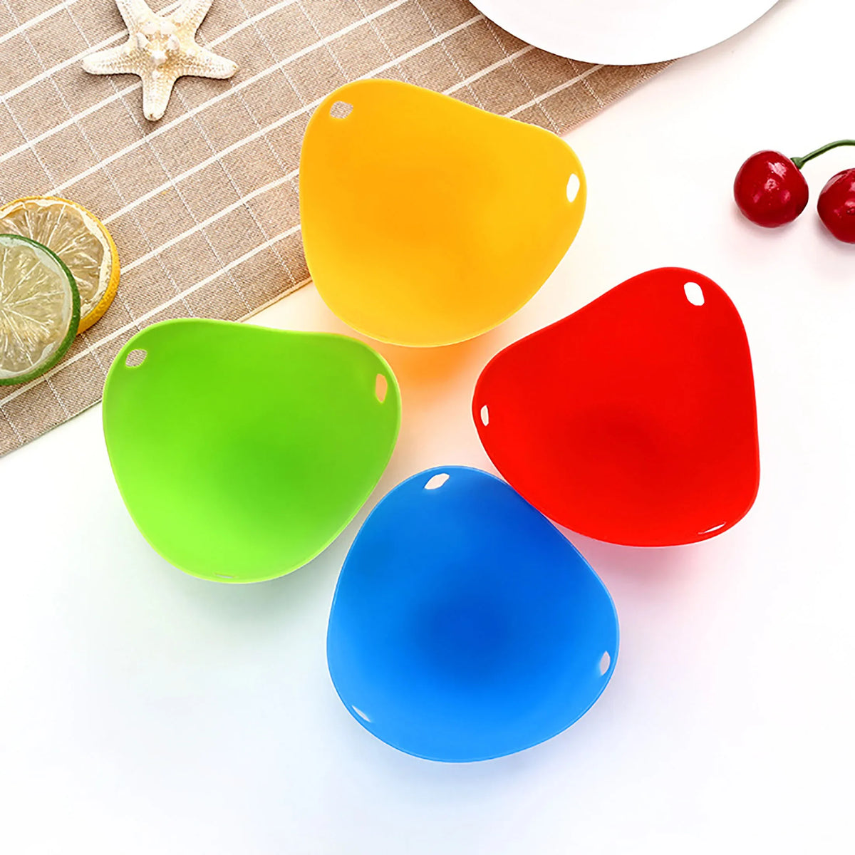 A set of colorful silicone egg poachers in yellow, green, red, and blue placed on a white surface.