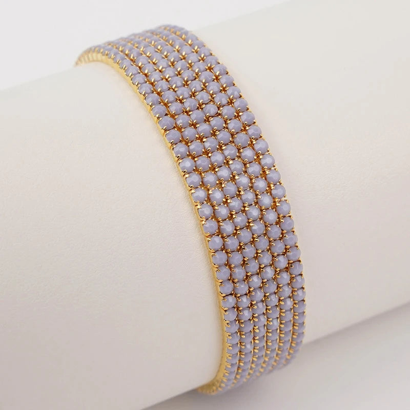 Gold stackable acrylic elastic bracelets with small white beads stacked on a wrist.