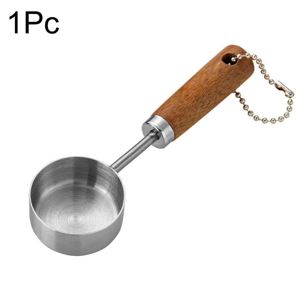 A single stainless steel measuring spoon with a wooden handle and chain for baking or bartending