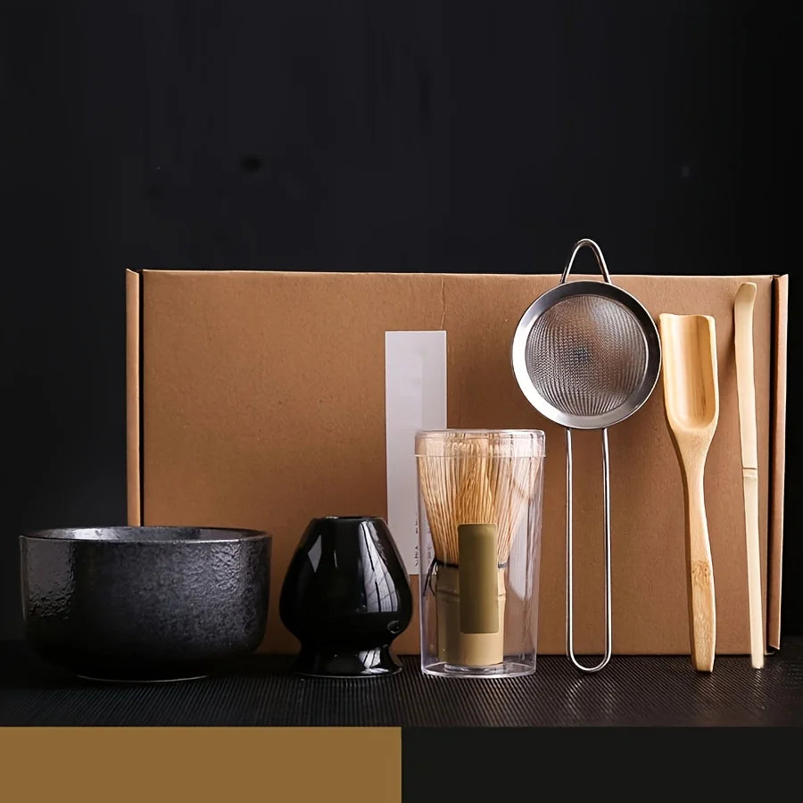 A traditional Japanese matcha tea set featuring a black bowl, dark ceramic vessel, and bamboo whisk and scoop on a brown card