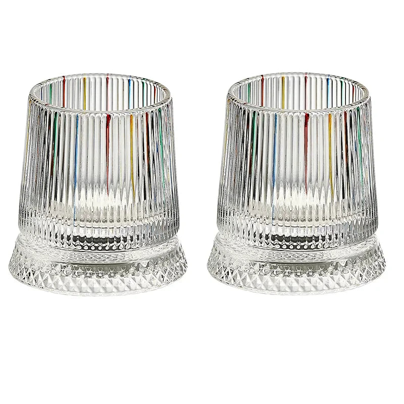 A pair of clear rotating whiskey glasses with multicolored vertical stripes and textured bases.