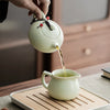 A hand pours tea from an elegant ceramic teapot into a cup on a wooden tray.
