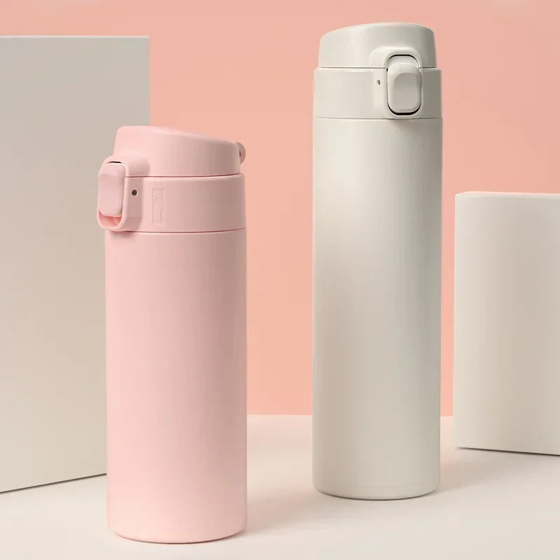 A pink insulated stainless steel vacuum flask standing next to a white one on a light surface.