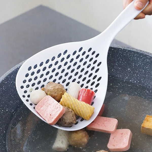 Eine weiße Küchensiebspatule schöpft verschiedene Speisen wie Fleischbällchen und Gemüse aus einem dunklen Topf.