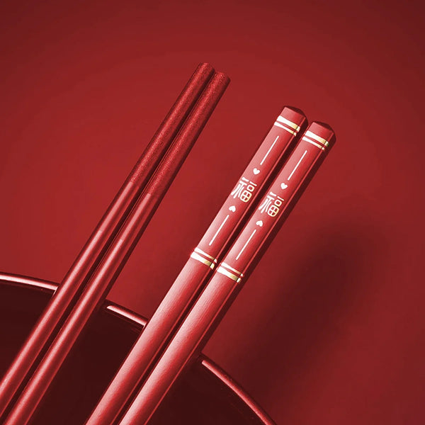 Ein Paar rote, goldverzierte Chopsticks auf einer dunklen Schale.
