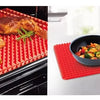 A silicone BBQ pizza mat is shown with roasted chicken pieces on a baking tray and a small skillet of food on a red mat.