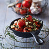 A black cast iron pan filled with roasted cherry tomatoes and herbs, resting on a wire rack.