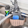 A gray hanging sponge rack with a blue holder and a green brush is placed in a stainless steel kitchen sink.